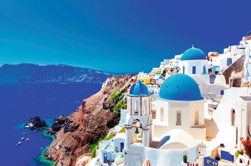 Santorini, A scenic view of a white and blue village on a cliff by the sea.