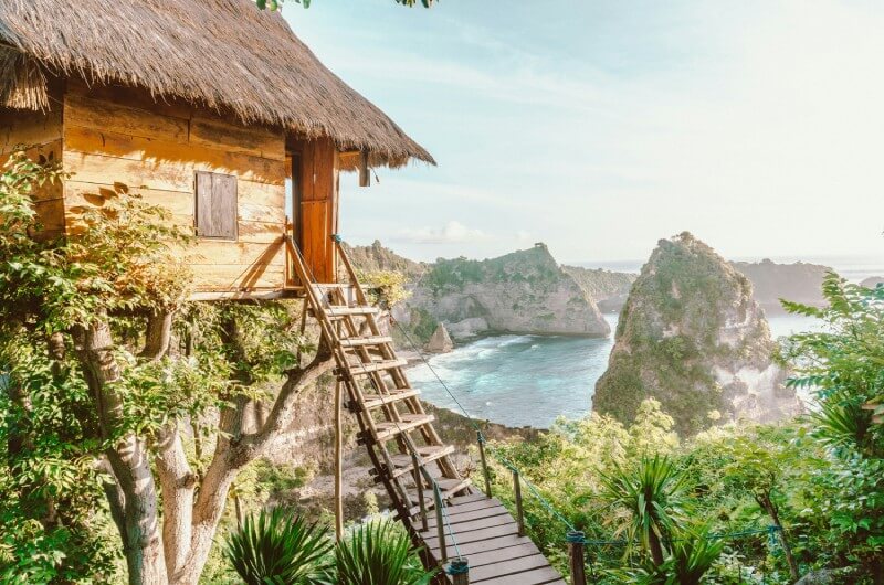 Bali-a-wooden-house-with-a-thatched-roof-next-to-a-body-of-water-johnny-africa-RGvbdyhsh_U-unsplash.A wooden hut on a cliff overlooking the ocean and the sky.A wooden hut on a cliff overlooking the ocean and the sky.